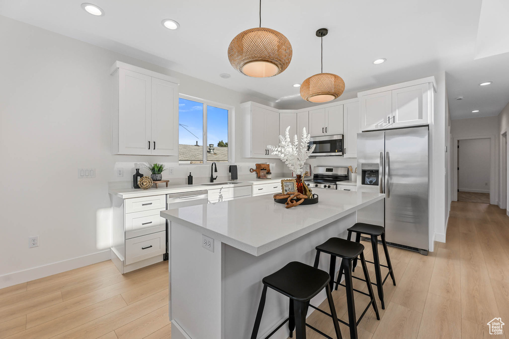 Kitchen with stainless steel appliances, a breakfast bar, light wood finished floors, recessed lighting, and white cabinetry