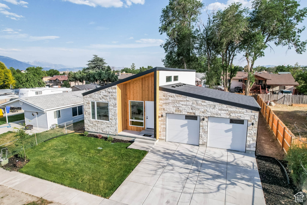 View of front facade with stone siding, driveway, an attached garage, a mountain view, and a residential view