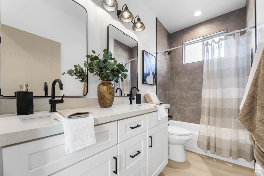 Bathroom featuring double vanity, shower / bath combo, wood finished floors, and recessed lighting