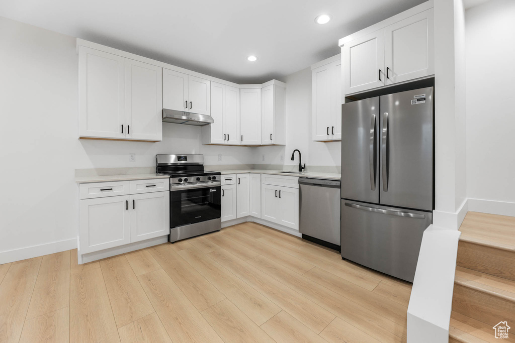 Kitchen featuring stainless steel appliances, under cabinet range hood, light countertops, white cabinets, and light wood-style floors
