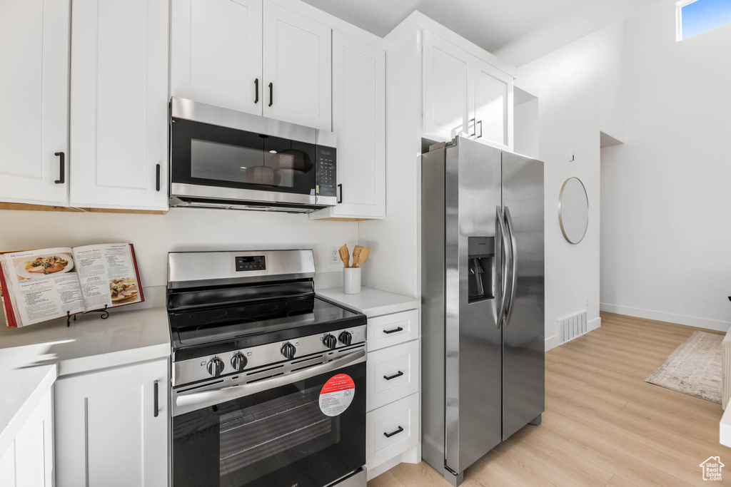 Kitchen with stainless steel appliances, light wood-style flooring, light countertops, and white cabinets