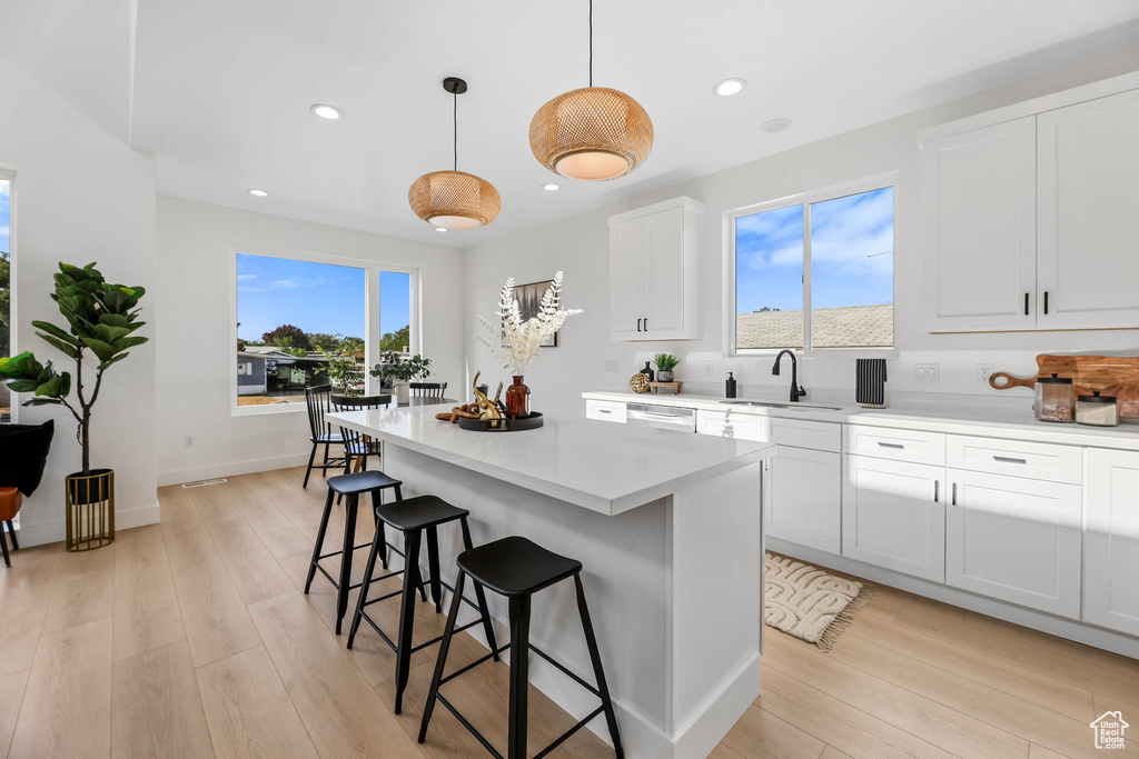 Kitchen featuring a breakfast bar, a center island, light countertops, light wood-type flooring, and recessed lighting