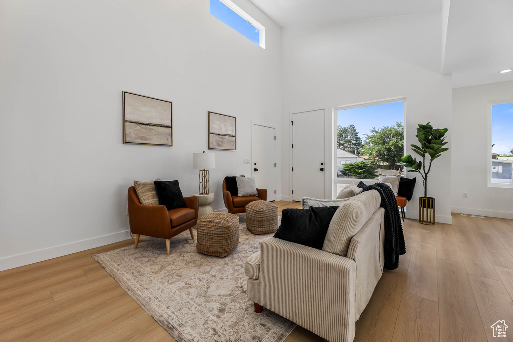 Living room featuring healthy amount of natural light, light wood-style flooring, and a towering ceiling