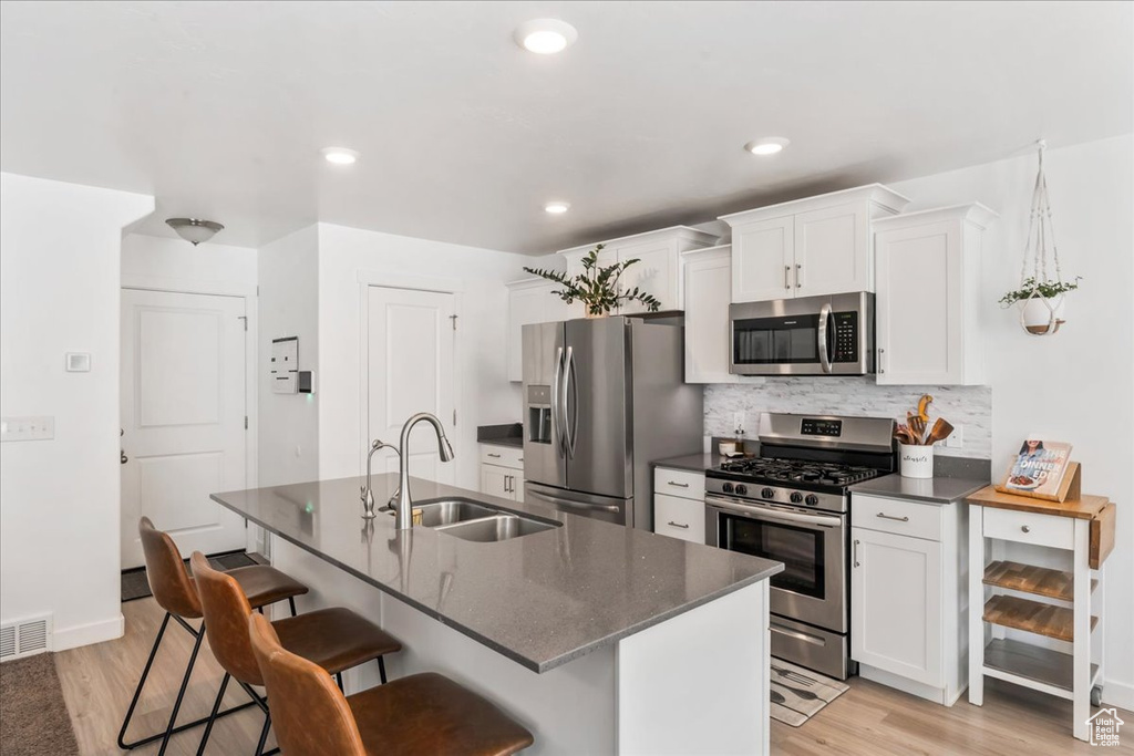 Kitchen featuring stainless steel appliances, a kitchen bar, decorative backsplash, light wood-style floors, and white cabinetry