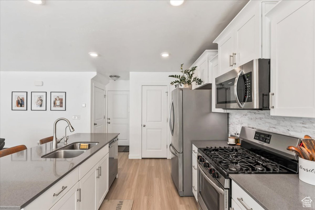 Kitchen featuring appliances with stainless steel finishes, white cabinets, light wood-style flooring, dark stone countertops, and tasteful backsplash