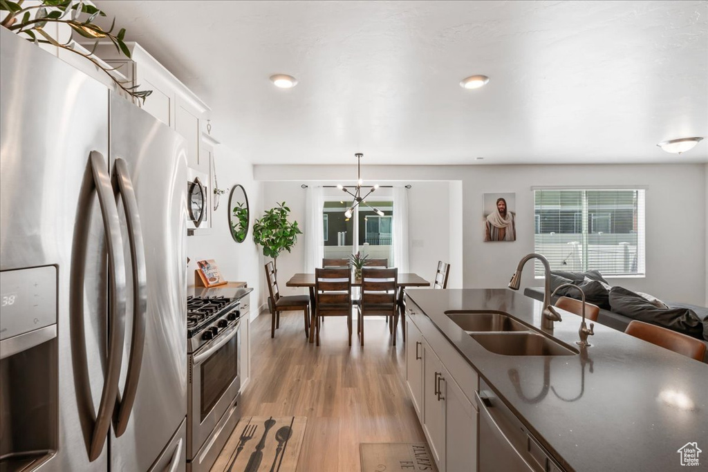 Kitchen featuring appliances with stainless steel finishes, dark countertops, light wood-style floors, white cabinets, and hanging light fixtures