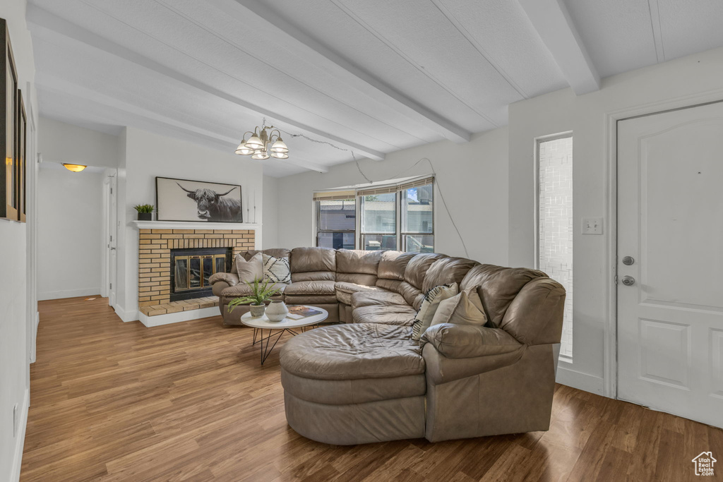 Living area featuring beam ceiling, wood finished floors, a brick fireplace, and a chandelier
