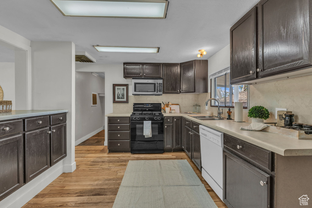 Kitchen featuring black gas range, stainless steel microwave, white dishwasher, and dark brown cabinets