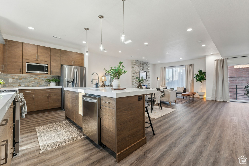 Kitchen featuring appliances with stainless steel finishes, wood finished floors, recessed lighting, decorative backsplash, and light countertops