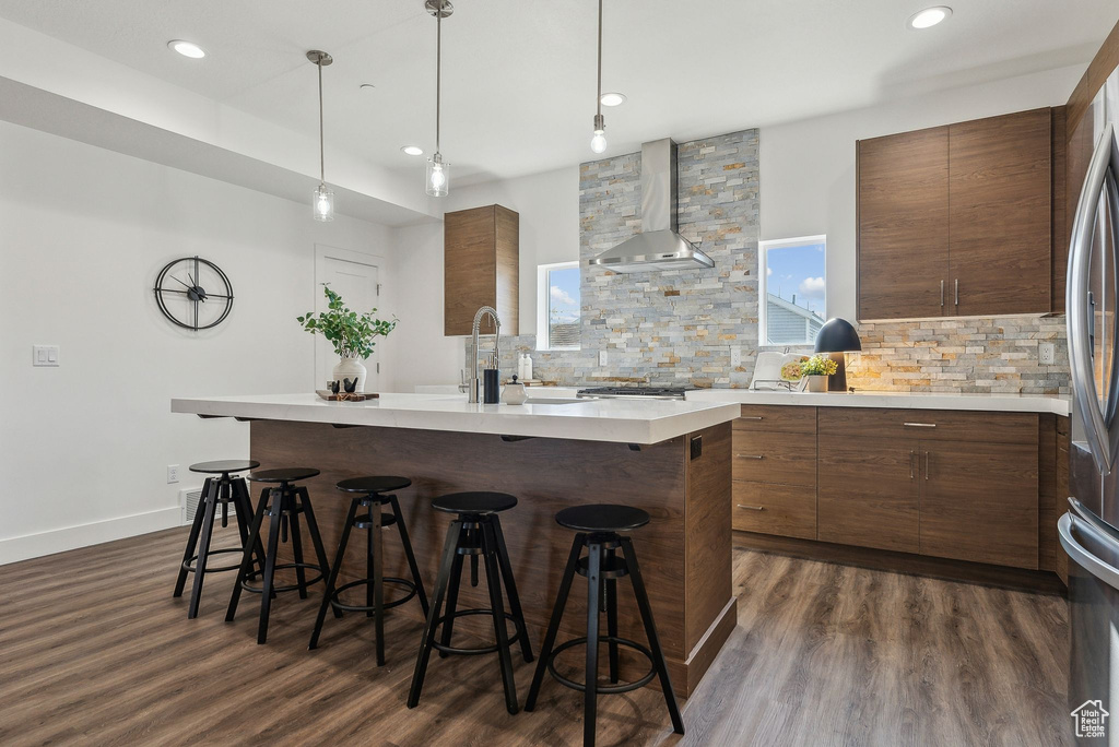 Kitchen featuring wall chimney exhaust hood, tasteful backsplash, a breakfast bar area, modern cabinets, and recessed lighting