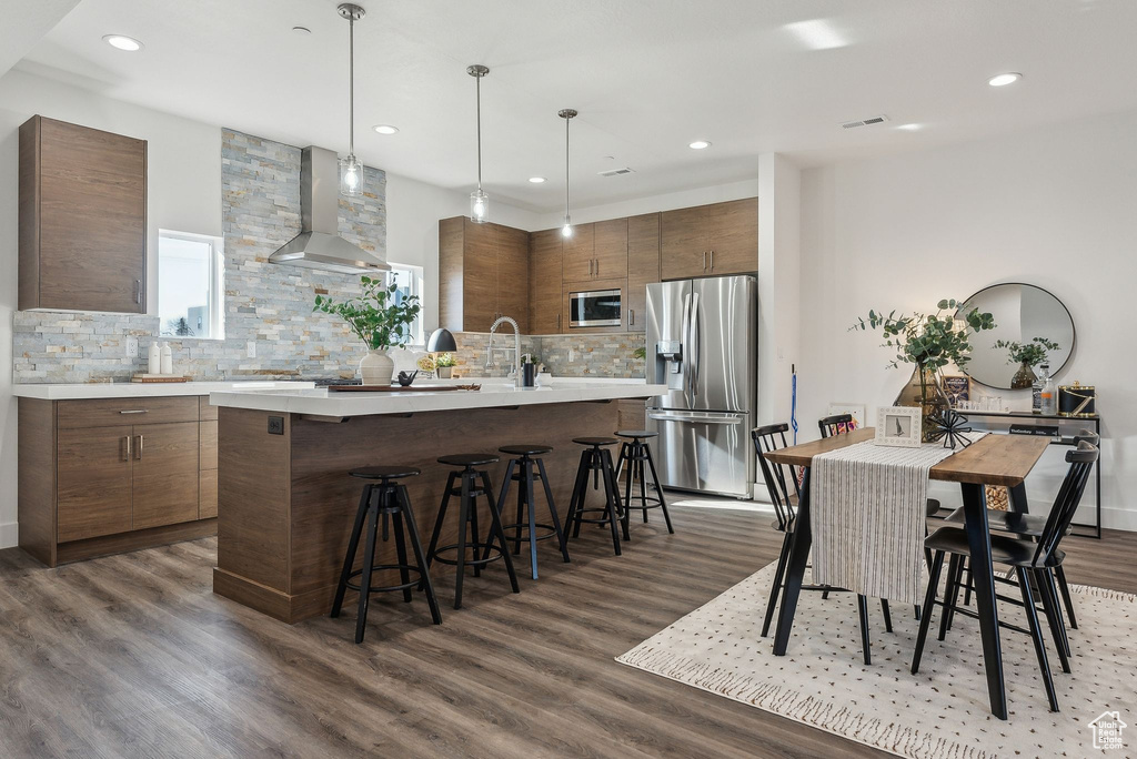 Kitchen with stainless steel appliances, wall chimney range hood, tasteful backsplash, a breakfast bar area, and light countertops