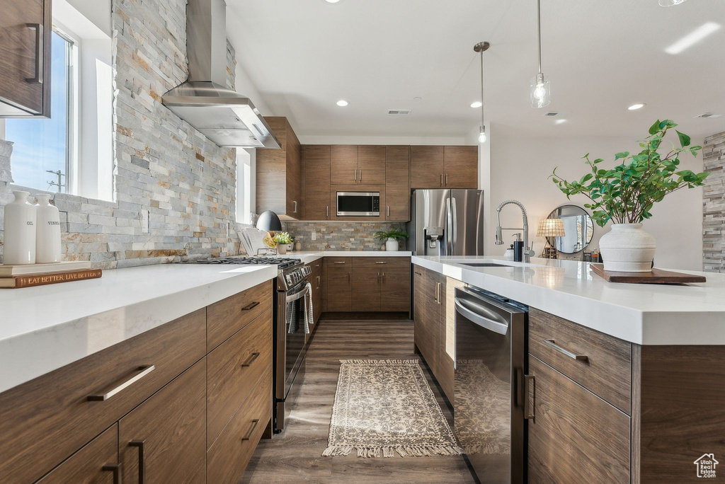 Kitchen with stainless steel appliances, range hood, tasteful backsplash, dark wood-style flooring, and light countertops