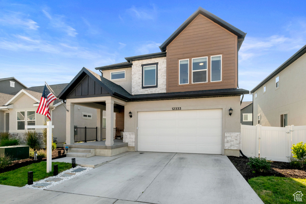 View of front of home featuring stone siding, a porch, concrete driveway, an attached garage, and board and batten siding