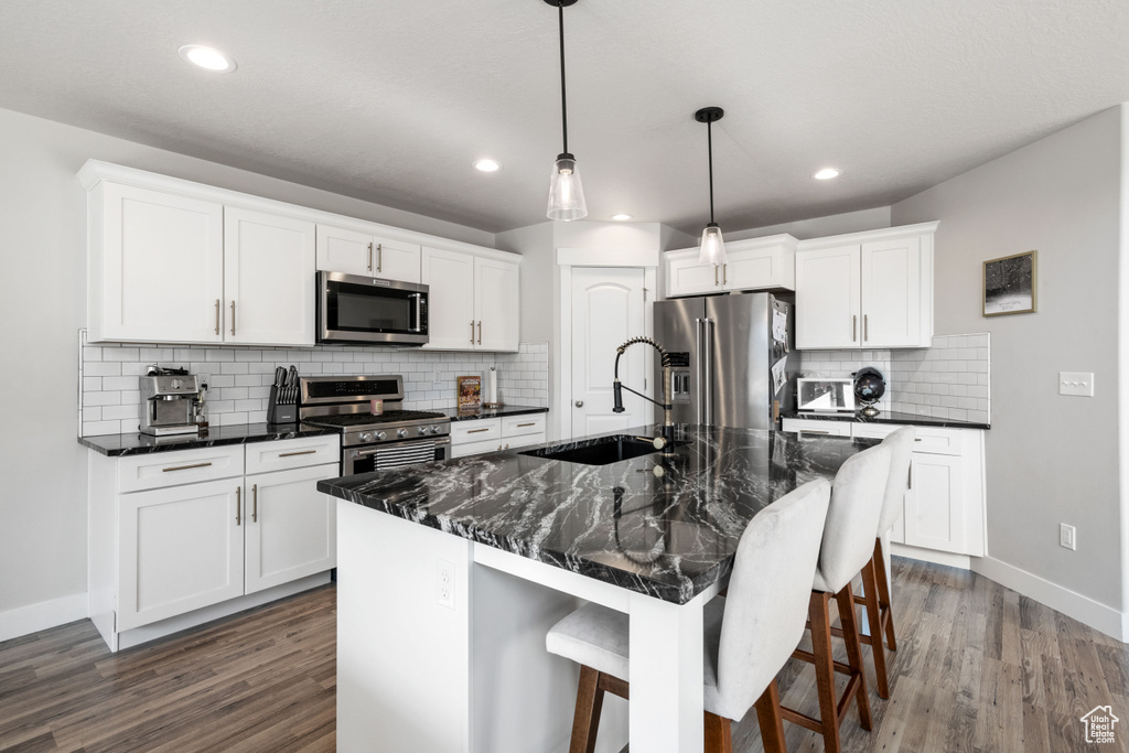 Kitchen featuring appliances with stainless steel finishes, dark wood finished floors, a breakfast bar, tasteful backsplash, and hanging light fixtures