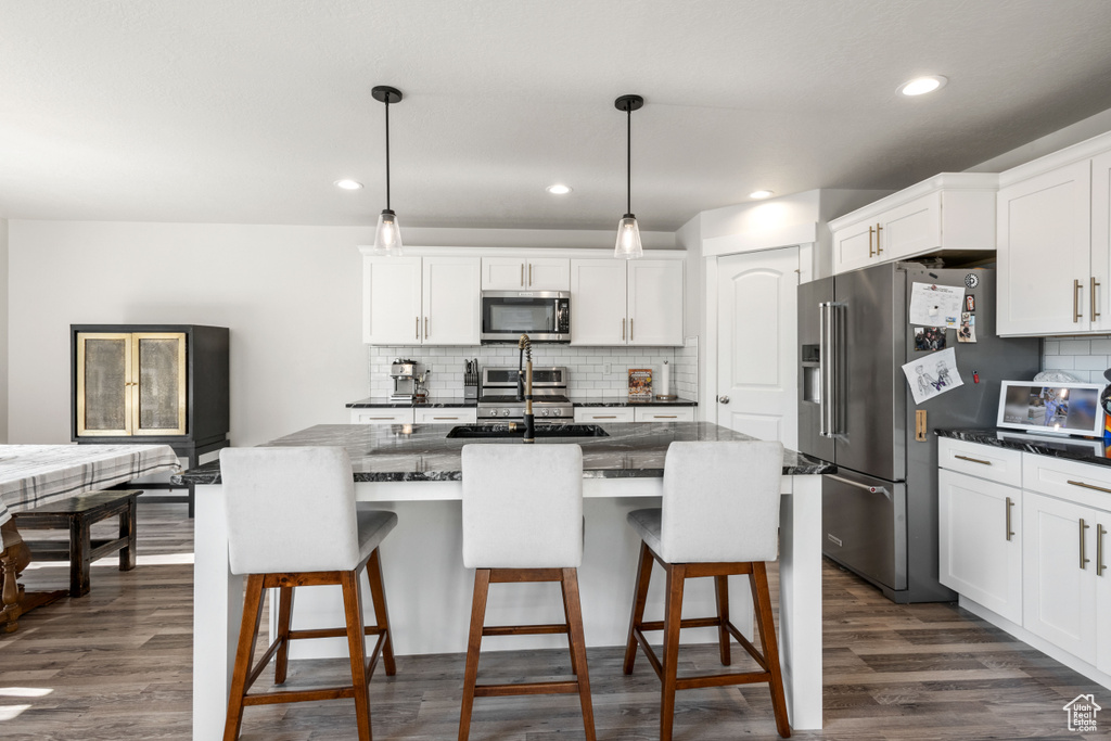 Kitchen with appliances with stainless steel finishes, backsplash, white cabinets, a kitchen bar, and recessed lighting