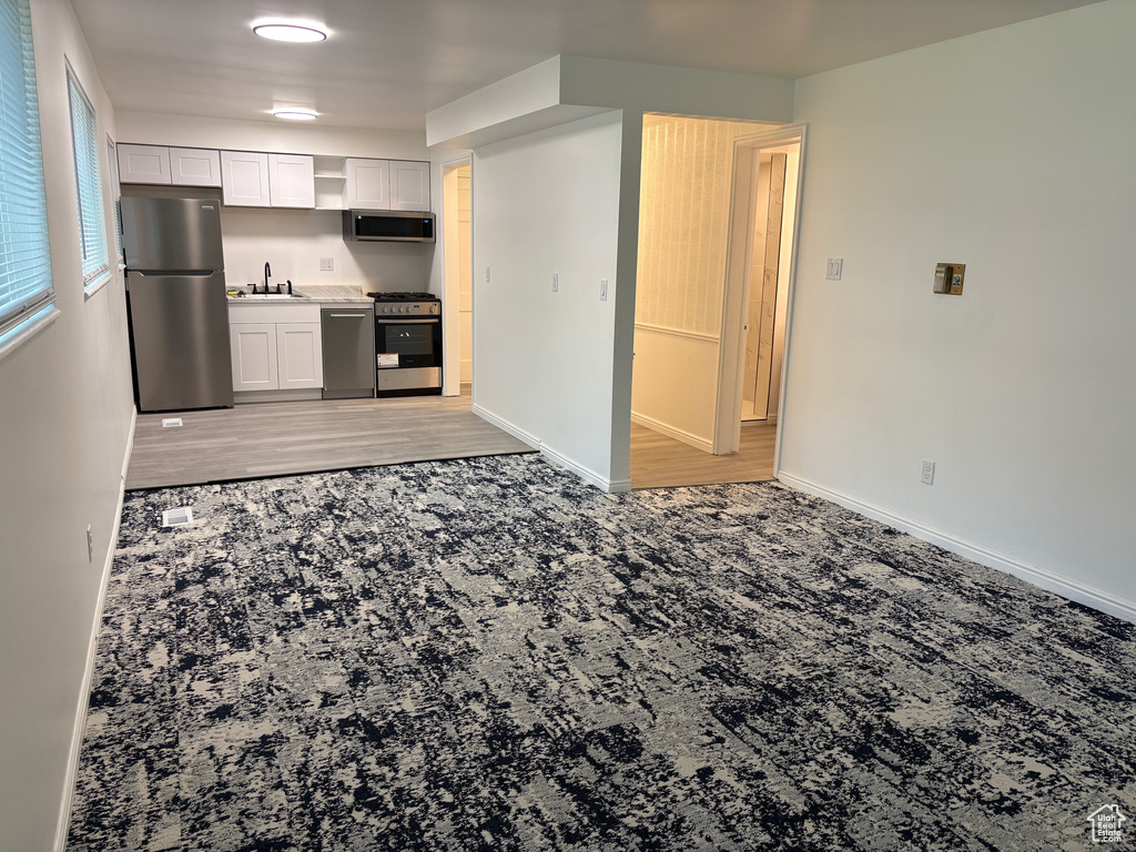 Kitchen featuring stainless steel appliances, open shelves, light colored carpet, white cabinetry, and light countertops