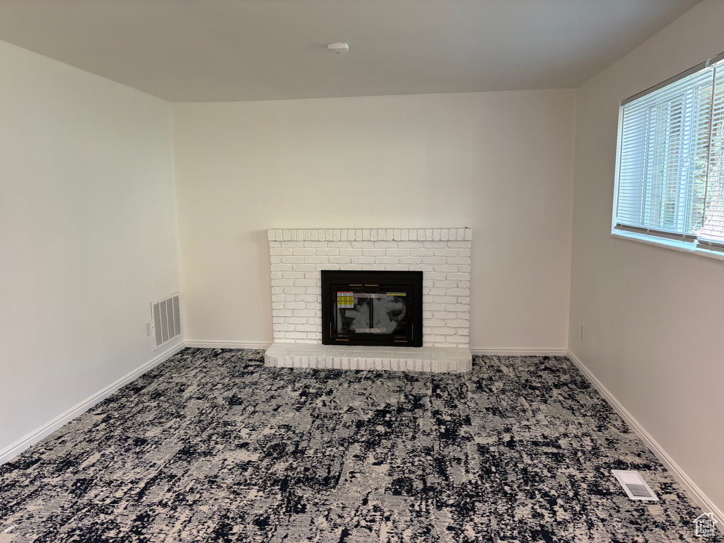 Unfurnished living room featuring carpet and a brick fireplace
