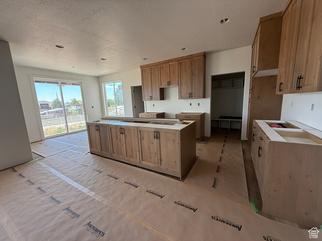 Kitchen with a textured ceiling, a center island, and brown cabinetry