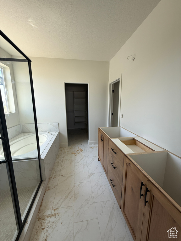 Full bathroom with marble finish floors, a bath, vanity, and a textured ceiling
