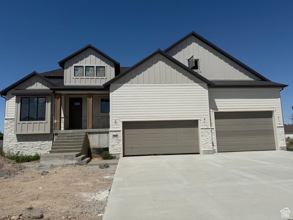 Modern farmhouse with board and batten siding, concrete driveway, an attached garage, covered porch, and stone siding