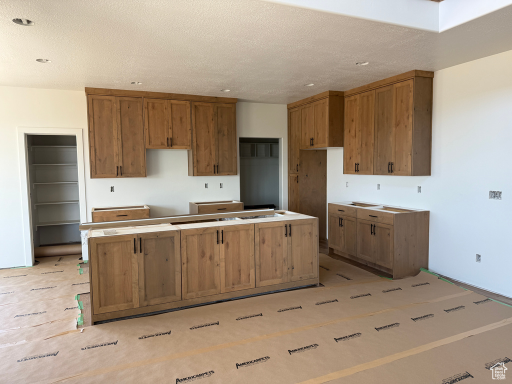 Kitchen featuring a kitchen island, brown cabinetry, a textured ceiling, and recessed lighting