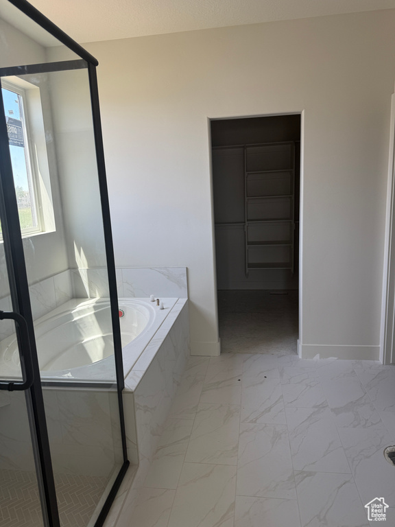 Bathroom featuring a bath, marble look tile flooring, and a stall shower
