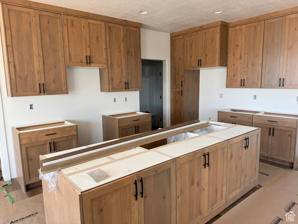 Kitchen with a textured ceiling, brown cabinetry, and a kitchen island