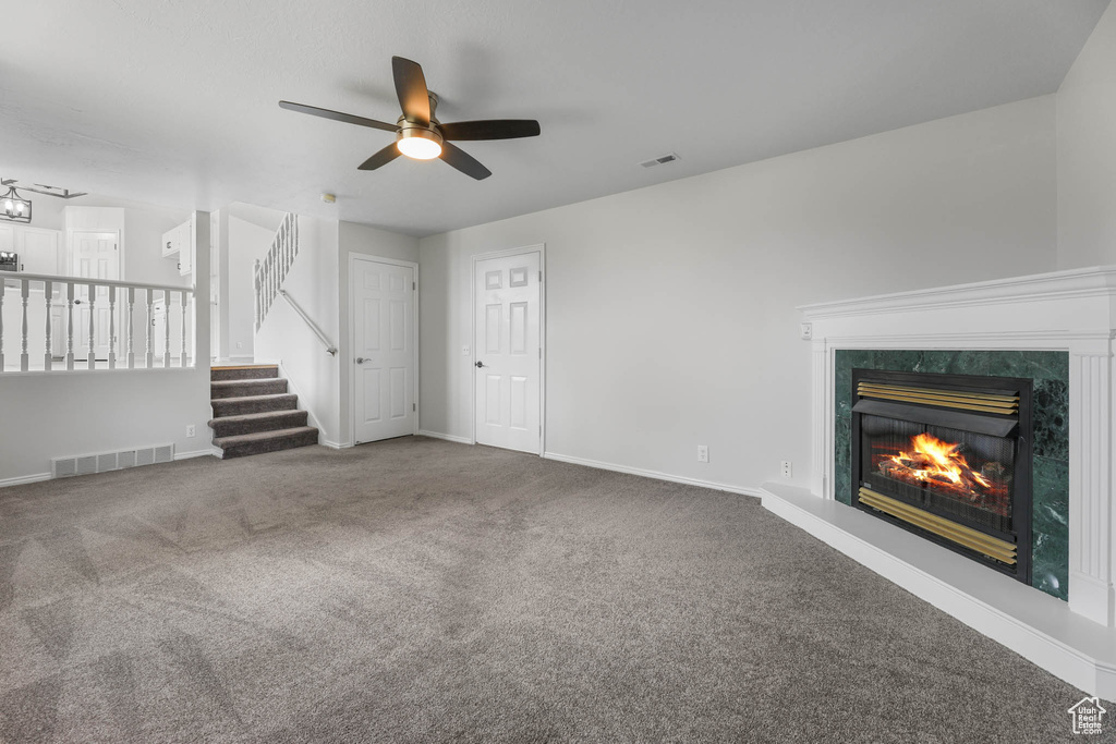 Unfurnished living room with ceiling fan, carpet flooring, a premium fireplace, and stairway