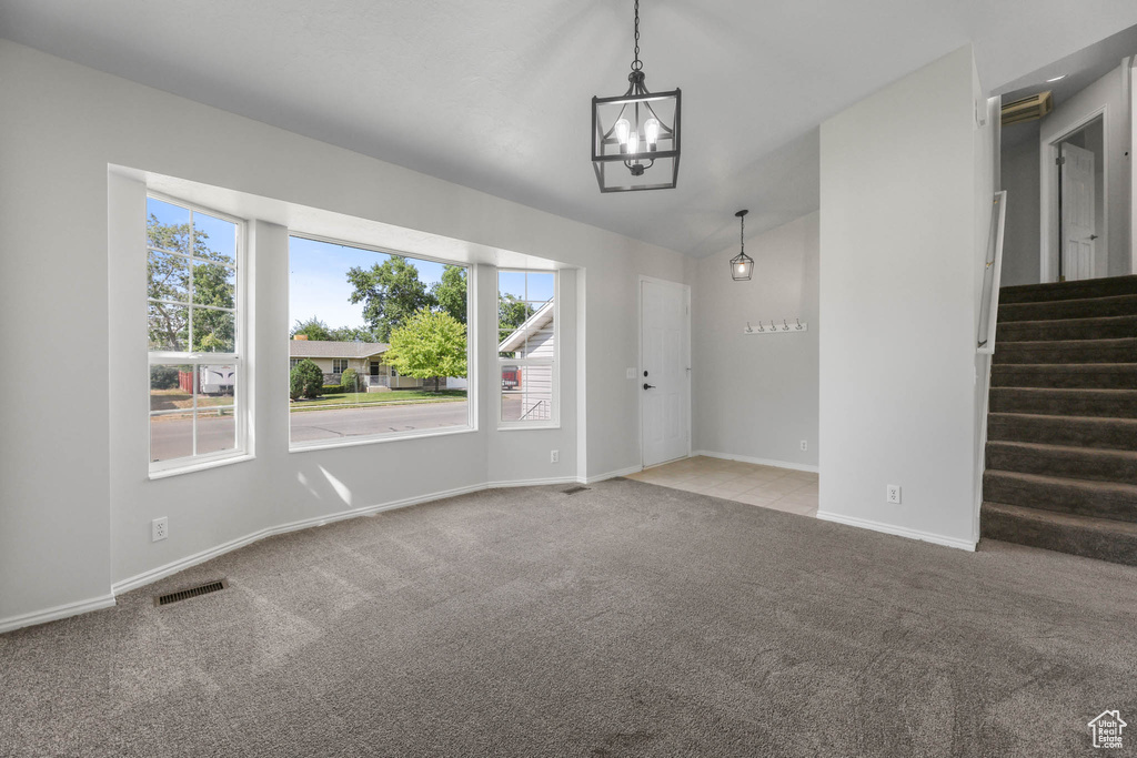 Unfurnished living room featuring a chandelier, carpet, vaulted ceiling, and stairway