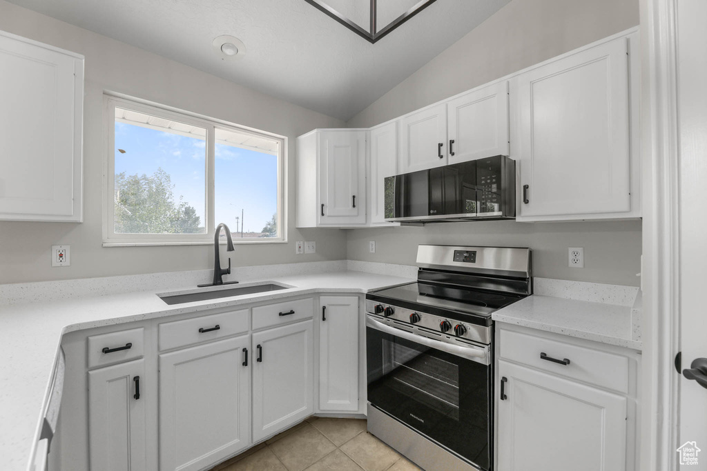 Kitchen with appliances with stainless steel finishes, vaulted ceiling, white cabinets, and light countertops
