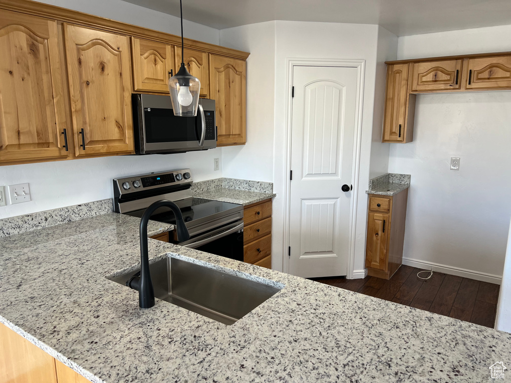 Kitchen featuring stainless steel appliances, light stone countertops, dark wood-style flooring, and brown cabinets