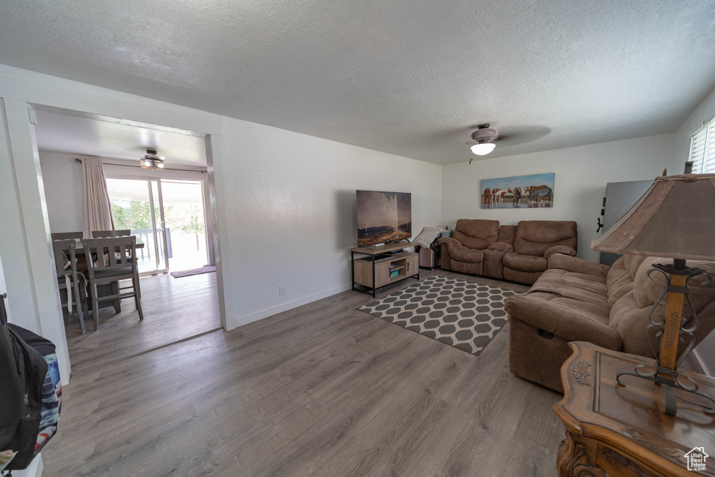 Living area with ceiling fan, wood finished floors, healthy amount of natural light, and a textured ceiling