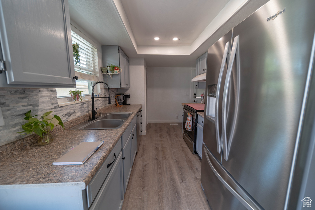 Kitchen with appliances with stainless steel finishes, backsplash, light wood-type flooring, a tray ceiling, and recessed lighting