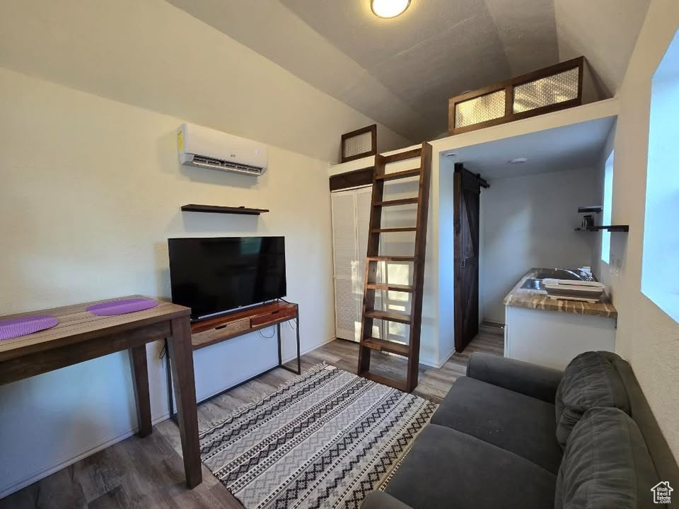 Living room featuring a wall mounted AC, wood finished floors, and vaulted ceiling