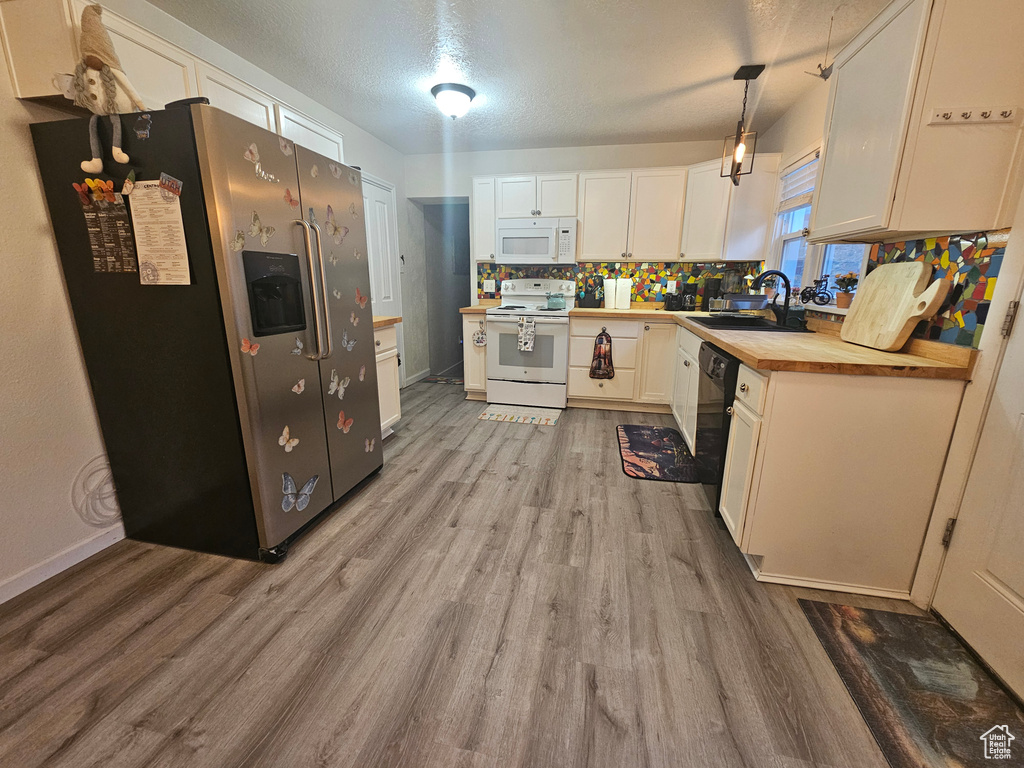 Kitchen with white appliances, light wood-type flooring, wooden counters, white cabinetry, and tasteful backsplash