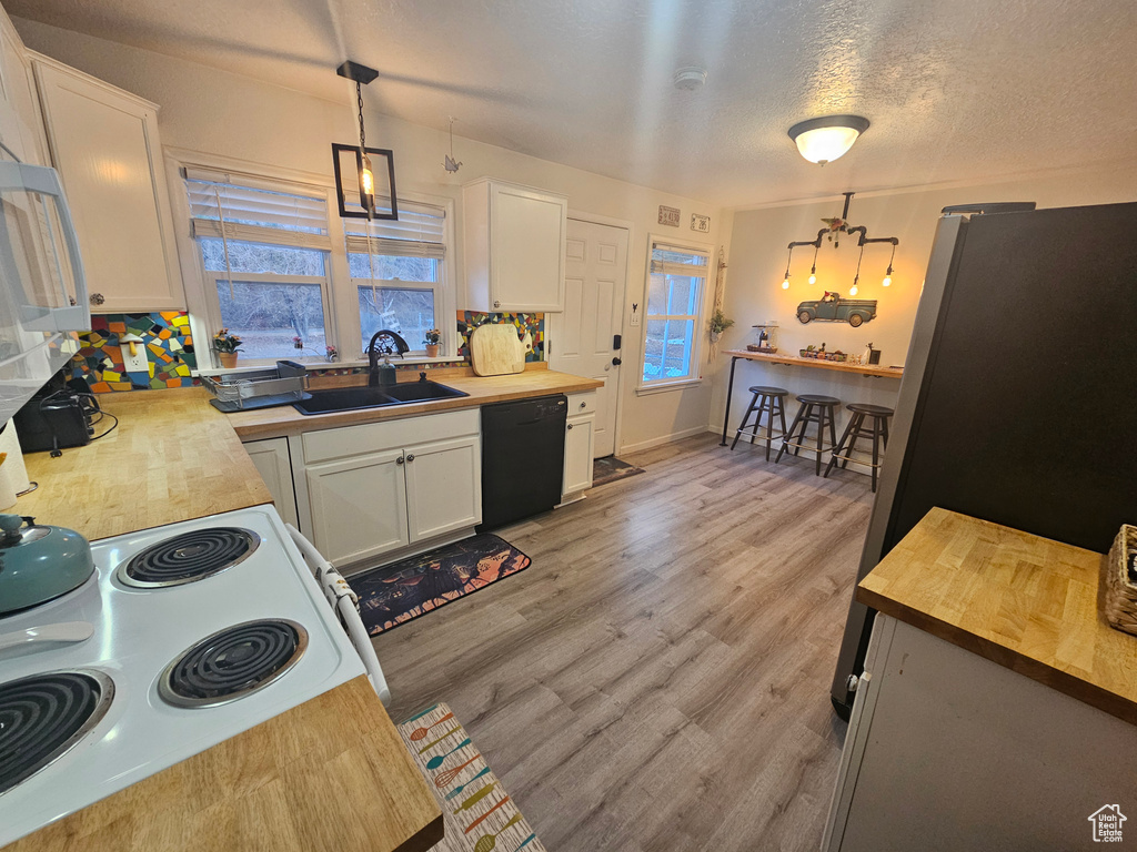 Kitchen featuring butcher block countertops, black dishwasher, freestanding refrigerator, white cabinets, and hanging light fixtures
