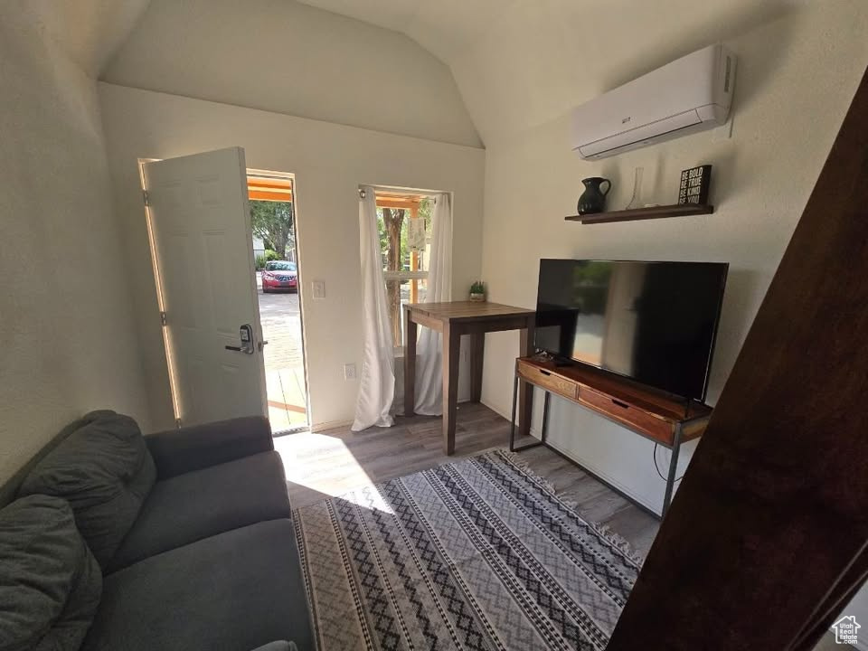 Living room with a wall mounted AC, wood finished floors, and vaulted ceiling
