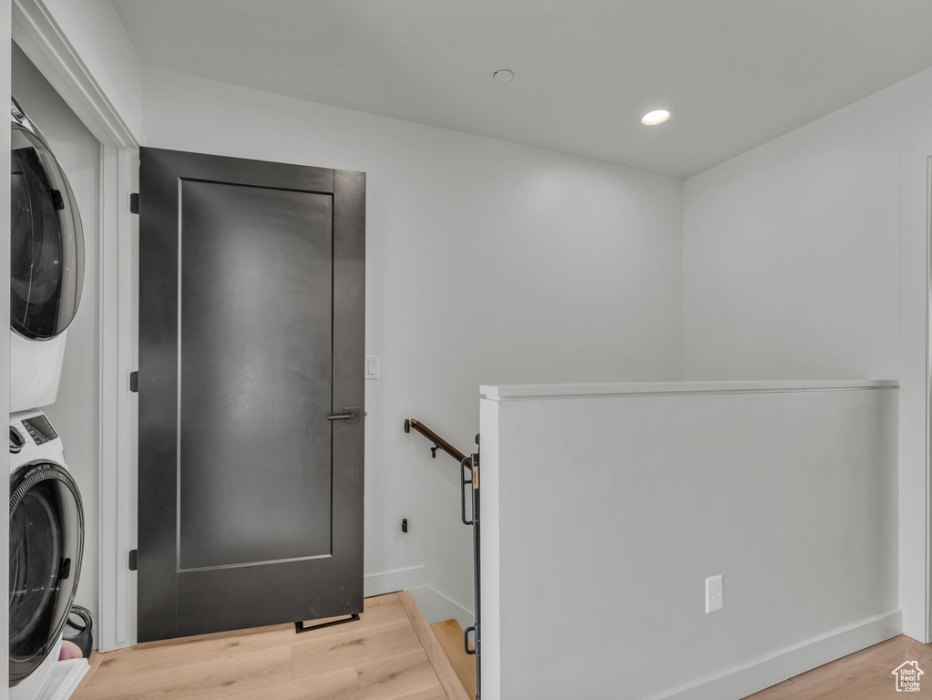 Washroom with stacked washing machine and dryer, light wood-style flooring, and recessed lighting