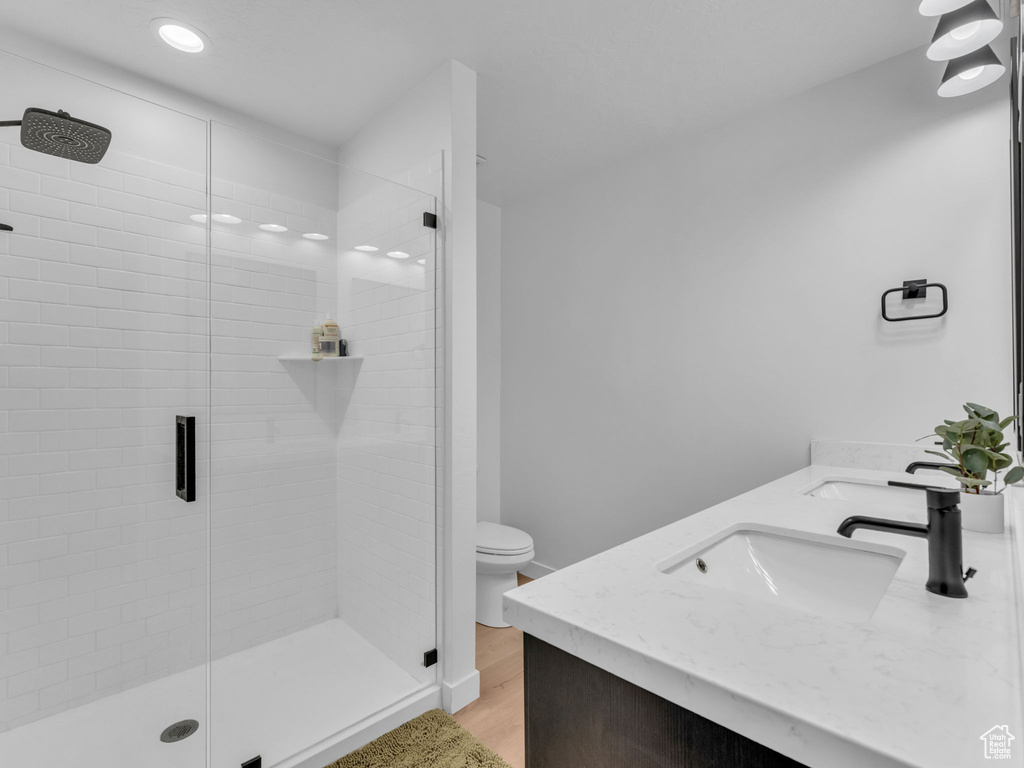 Full bath with double vanity, a stall shower, wood finished floors, and recessed lighting