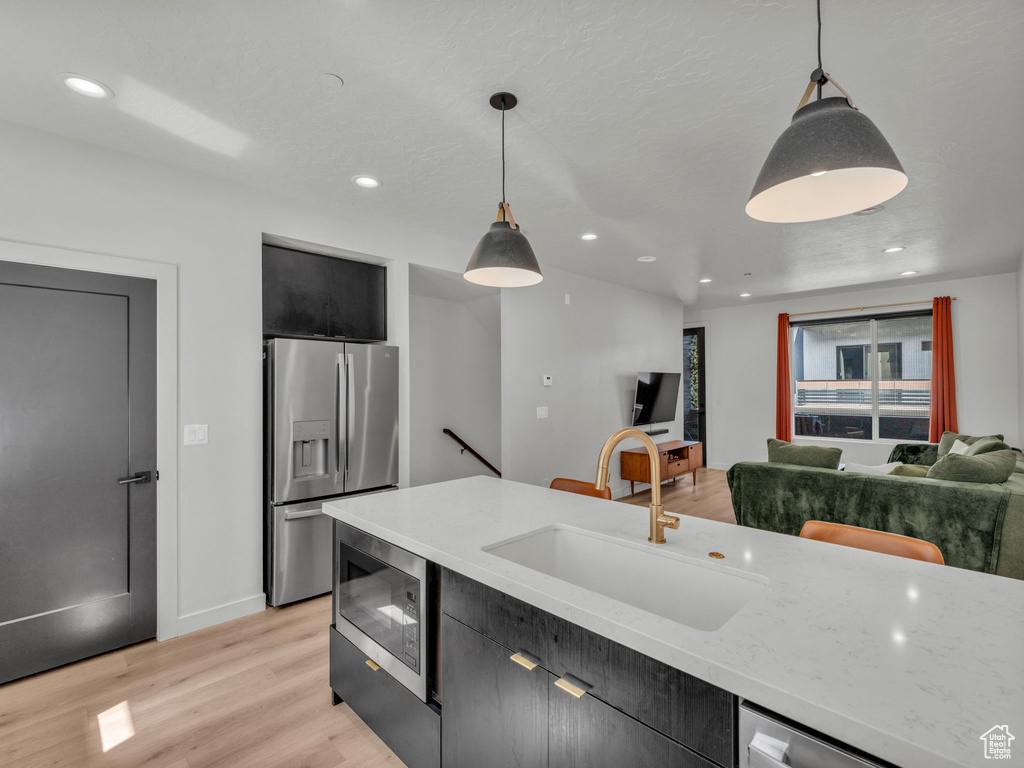 Kitchen with stainless steel appliances, dark cabinets, decorative light fixtures, light wood-type flooring, and recessed lighting