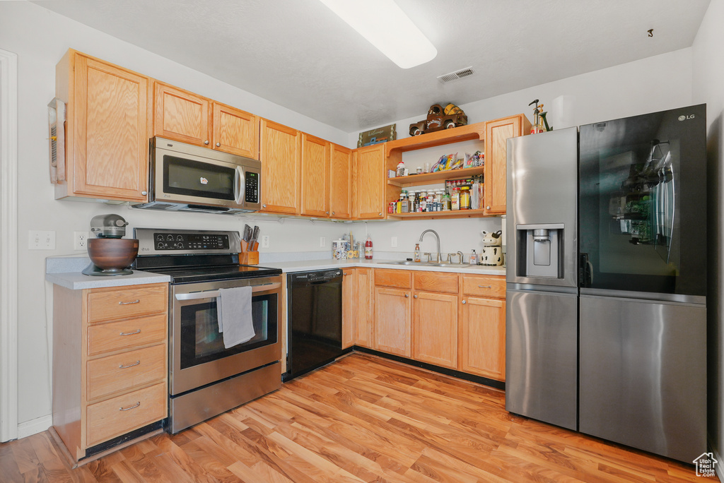 Kitchen with appliances with stainless steel finishes, open shelves, light countertops, and light wood-style flooring