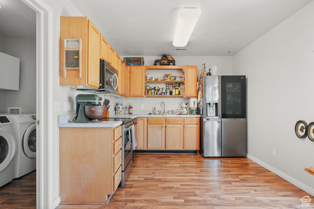 Kitchen with stainless steel appliances, washing machine and clothes dryer, light wood finished floors, light countertops, and light brown cabinets