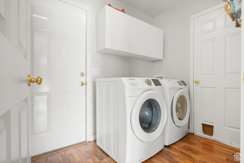 Washroom featuring cabinet space, washing machine and dryer, and wood finished floors