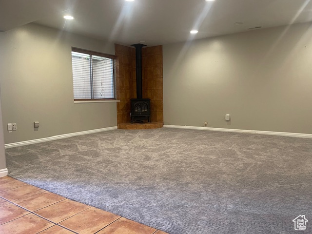 Unfurnished living room with a wood stove, carpet, tile patterned floors, and recessed lighting