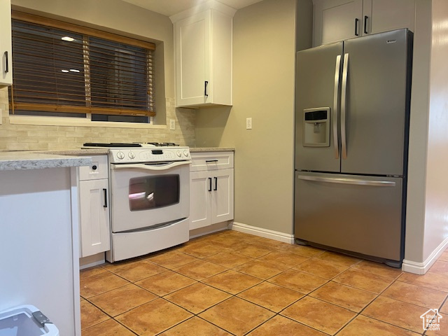 Kitchen featuring stainless steel fridge with ice dispenser, white range oven, decorative backsplash, white cabinetry, and light tile patterned floors