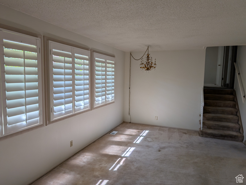 Unfurnished dining area featuring carpet, a textured ceiling, stairway, and a chandelier