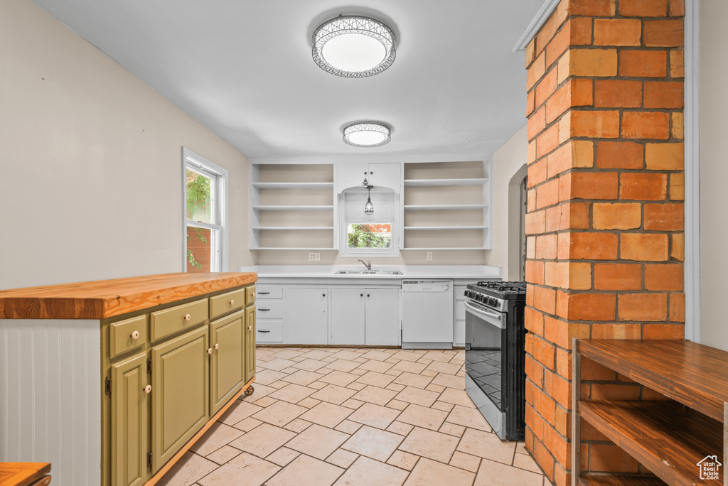 Kitchen with white dishwasher, stainless steel gas range, open shelves, wooden counters, and green cabinets