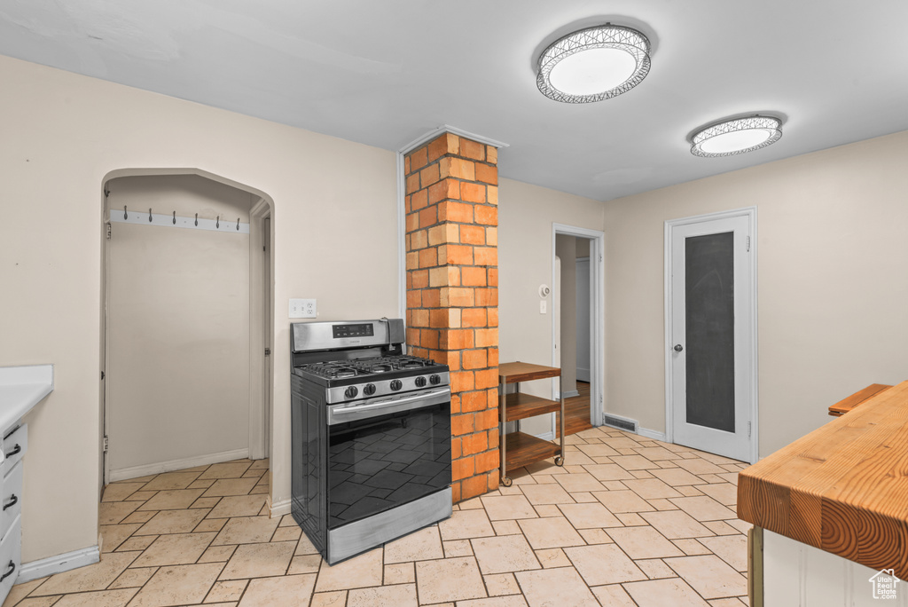 Kitchen featuring gas stove, arched walkways, butcher block counters, and white cabinetry