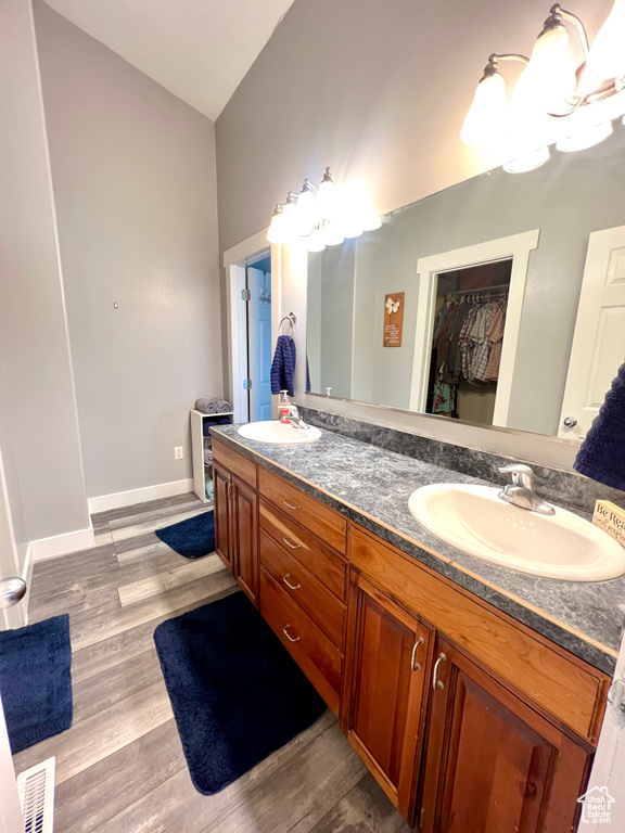 Bathroom with double vanity, wood finished floors, a walk in closet, and vaulted ceiling