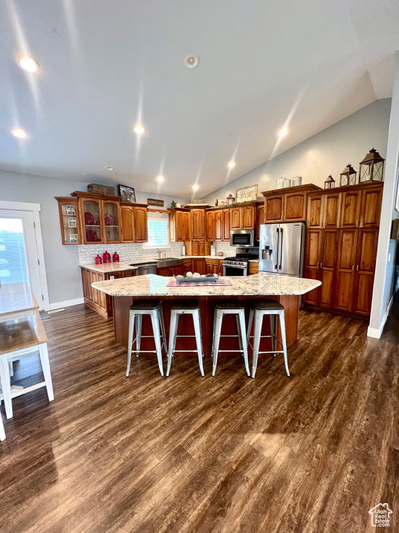 Kitchen featuring appliances with stainless steel finishes, a spacious island, a kitchen breakfast bar, dark wood-style floors, and vaulted ceiling